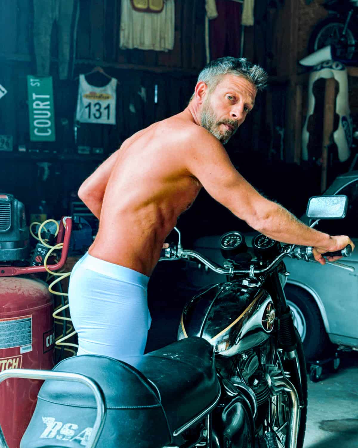 Man sitting on a motorcycle in a garage with various items in the background