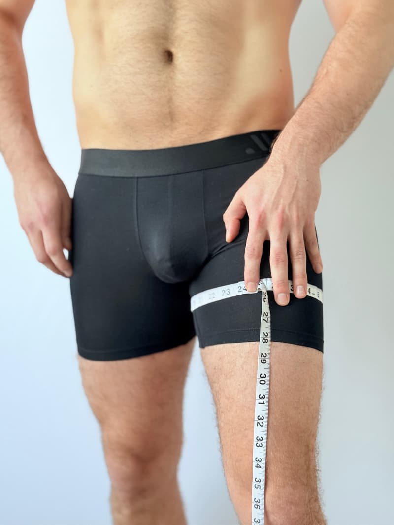 Person wearing black boxer briefs with a measuring tape around the waist on a light gray background