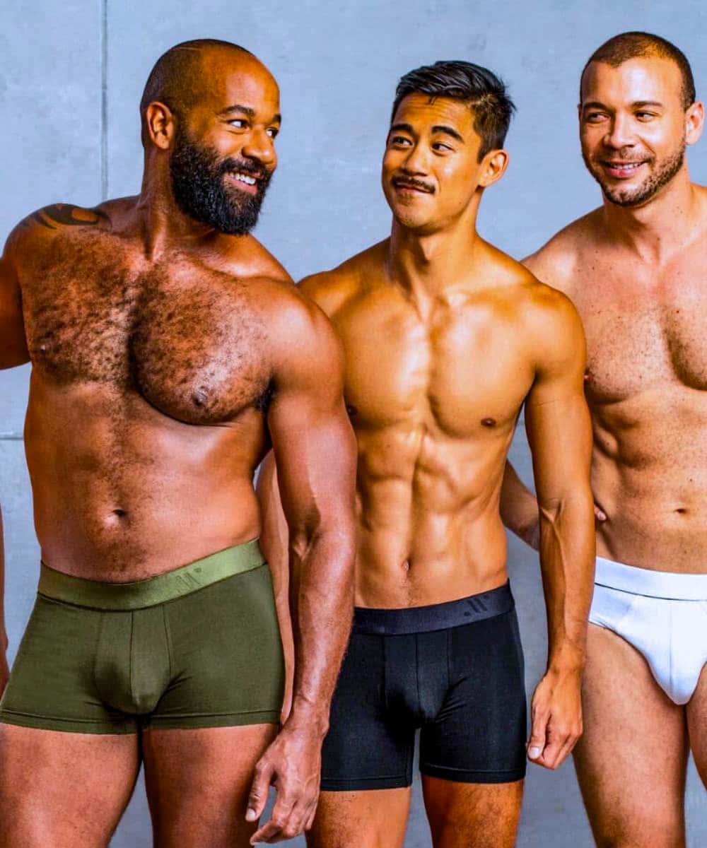 Three men wearing underwear standing side by side against a gray background