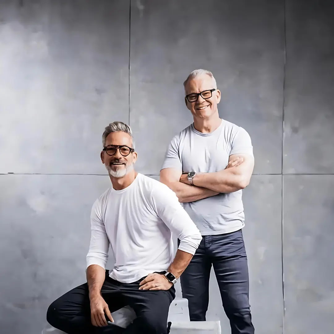 ALPHX founders Tom Speight and Garrett Swann – two longtime friends and fashion industry veterans – smiling in white t-shirts and jeans.