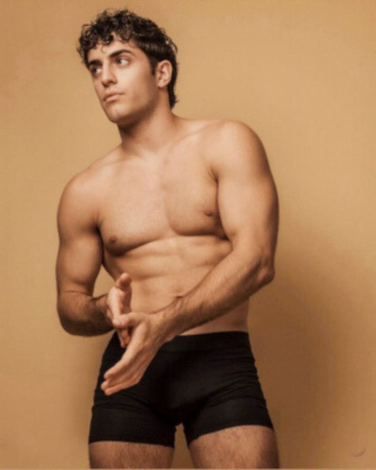 Confident male model stands against a tan backdrop wearing black ALPHX boxer briefs, highlighting the supportive fit and athletic cut designed for modern comfort.
