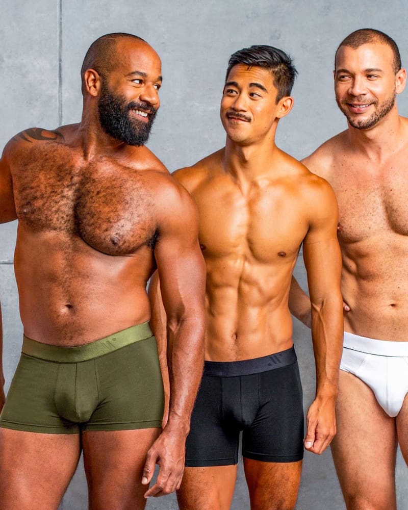Three men wearing underwear standing side by side against a gray background
