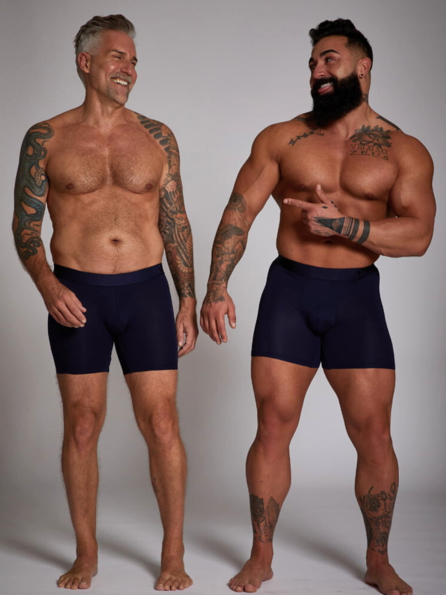 Two men wearing navy blue boxer briefs against a plain background