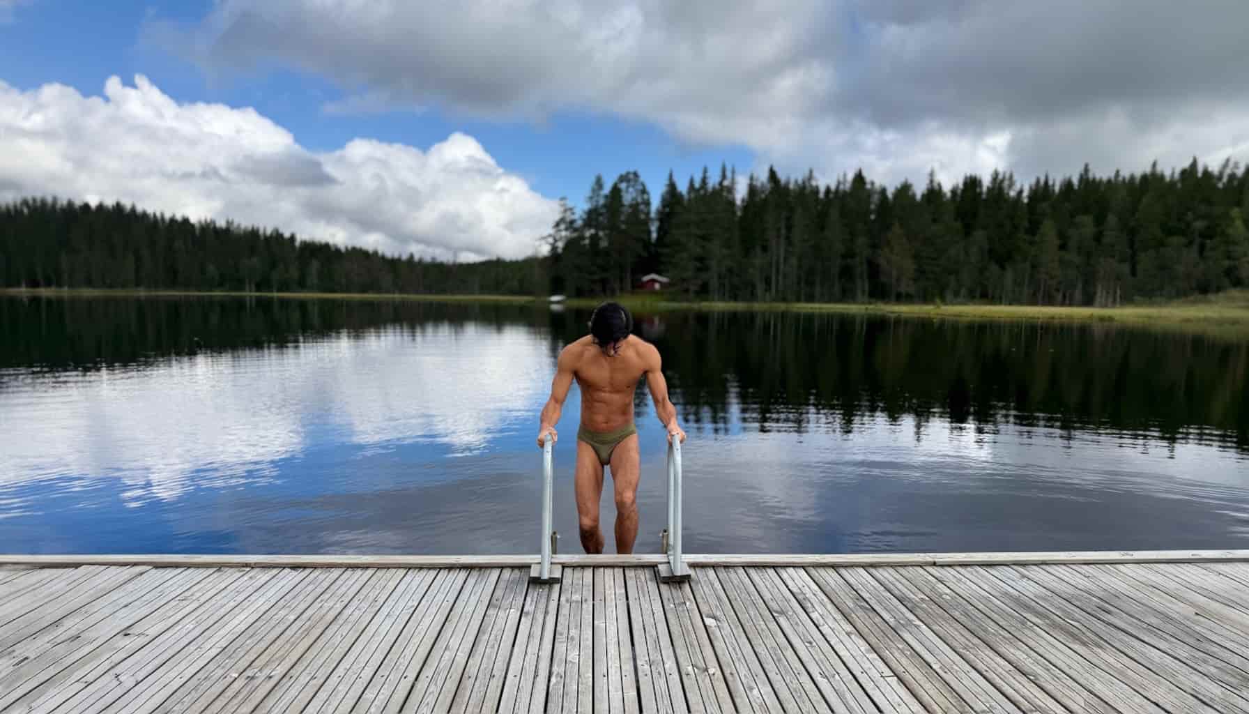 Man standing on a dock over a lake with trees in the background wearing green alphx briefs