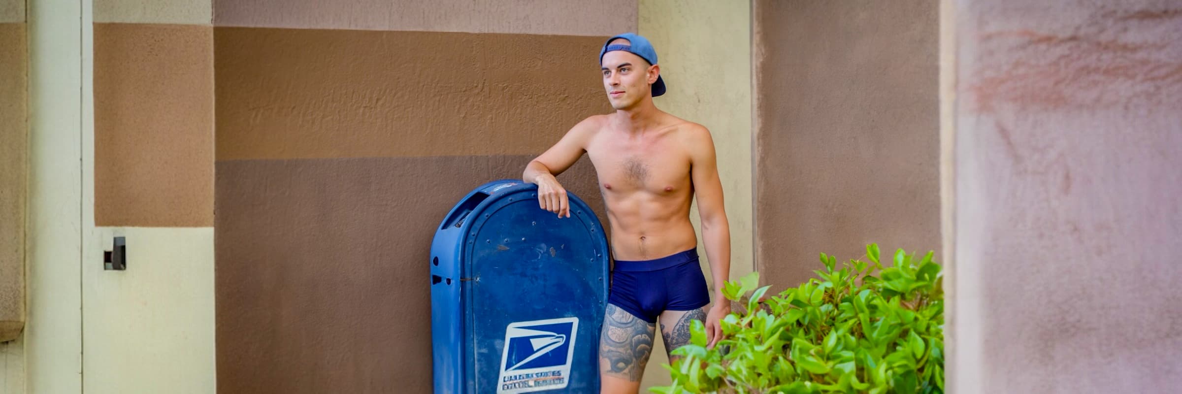 Man holding a blue mailbox with a visible logo against a wall.