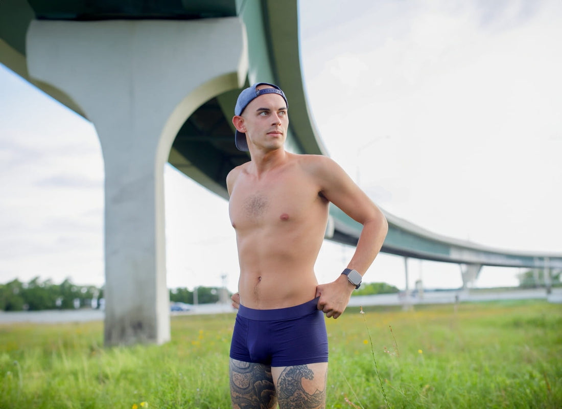 Model wearing ALPHX Maritime Navy Trunk in a field under an overpass—featuring a modern fit and athletic silhouette in a natural urban setting.
